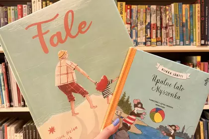 Książki „Fale” i „Upalne lato Myszonka” prezentowane przed bibliotecznym regałem.