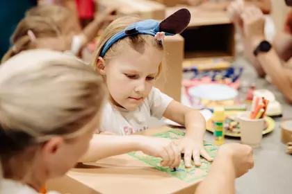 Dziecko ozdabia kartonowe pudełko przy pomocy szablonu.