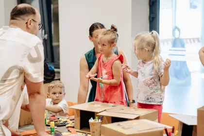 Dzieci i opiekunowie wspólnie tworzą kartonowe prace plastyczne.