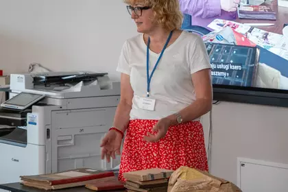 Małgorzata Gendera prezentuje zabytkowe księgi i dokumenty.