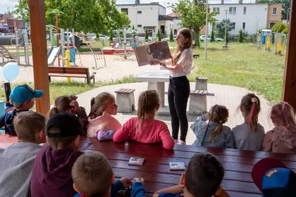 Dzieci słuchają głośnego czytania podczas wakacyjnych zajęć Bajkomotywy.