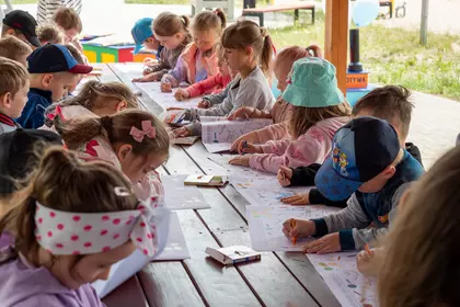 Dzieci wspólnie kolorują ilustracje przy długim stole.