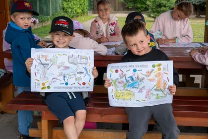 Uśmiechnięte dzieci prezentują pokolorowane prace wykonane na zajęciach.