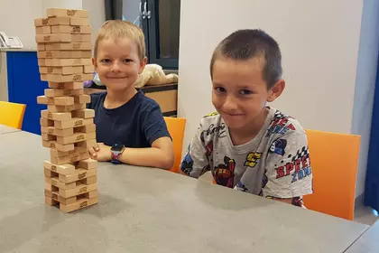 Dwaj chłopcy prezentują wysoką wieżę z klocków Jenga.