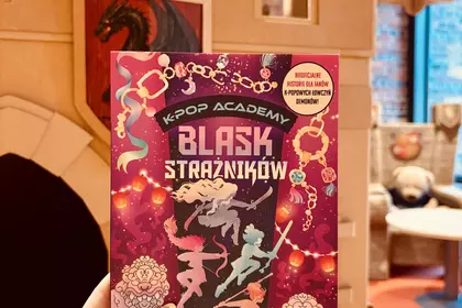 Książka „K-Pop Academy. Blask Strażników” na tle bibliotecznego zamku.
