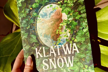 Książka „Klątwa Snow” na tle zielonych liści.