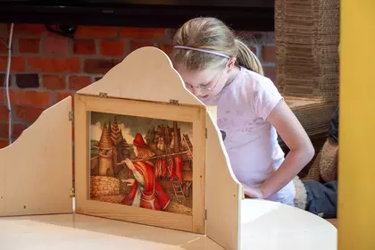 Dziewczynka odczytuje tekst do ilustracji w teatrzyku kamishibai.