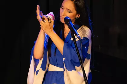 Dorota Miśkiewicz śpiewa, trzymając niewielki instrument perkusyjny.