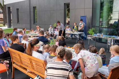 Dzieci uczestniczą w warsztatach o ziołach na tarasie biblioteki.