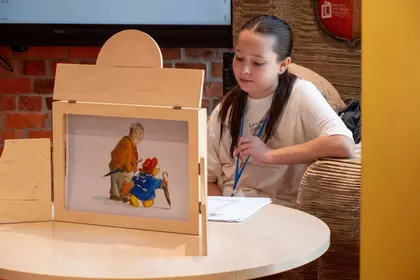 Dziewczynka prezentuje teatrzyk kamishibai z ilustracjami do przygód misia Paddingtona.
