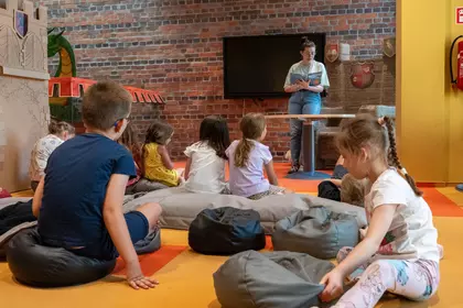 Dzieci słuchają opowieści z książki podczas wakacyjnych zajęć w bibliotece.