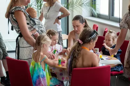 Dzieci i opiekunowie wykonują papierowe ptasie domki podczas warsztatów plastycznych.