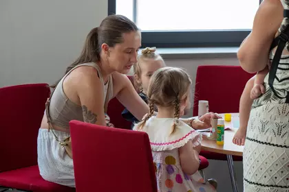 Opiekunka pomaga dzieciom podczas kreatywnych warsztatów plastycznych.