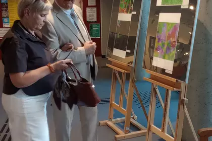 Para odwiedzających skupiona na oglądaniu prac wyeksponowanych przy oknie.