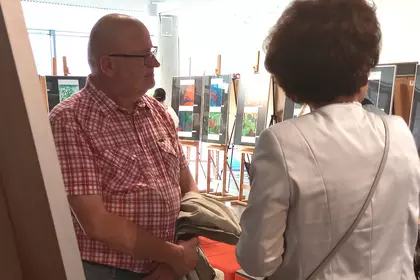 Mężczyzna w koszuli w kratę rozmawiający z kobietą na wystawie sztuki.