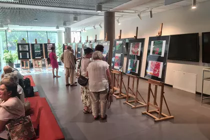Grupa gości z bliska ogląda kolorowe, abstrakcyjne prace na sztalugach w galerii.