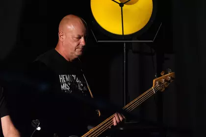 Basista gra na gitarze basowej w świetle scenicznym.