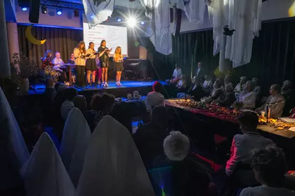 Szerokie ujęcie sali: młodzież czyta na scenie, a publiczność słucha wśród dekoracji.