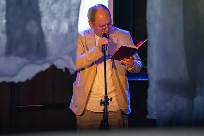 Mężczyzna czyta książkę do mikrofonu na scenie.