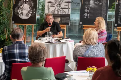 Spotkanie autorskie w przestrzeni biblioteki, dwójka gości rozmawia przed publiką.