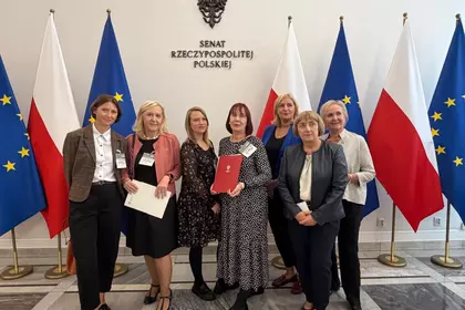 Grupa uczestników wydarzenia na tle polskich i unijnych flag.