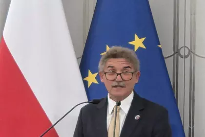 Senator przemawia przy mównicy na tle polskich i unijnych flag.