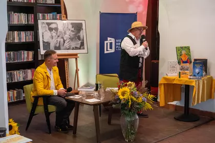 Dwóch prowadzących uczestniczy w rozmowie przy stoliku.