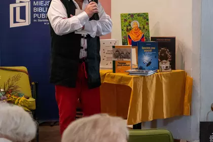 Mężczyzna mówi do publiczności przy stoliku z książkami o pszczołach.