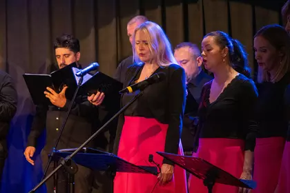 Wokalistki i wokaliści Cantus podczas koncertu przy pulpitach z nutami.