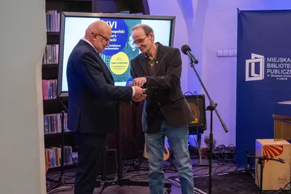 Syn Stanisława Grochowiaka przekazuje dokumenty Dyrektorowi biblioteki na scenie.