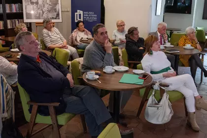 Uczestnicy spotkania siedzą przy stolikach w Bibliotece Ratuszowej.